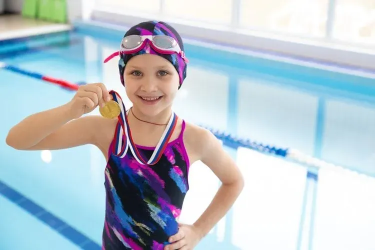little swimmer girl in swimming pool with medal for the first place