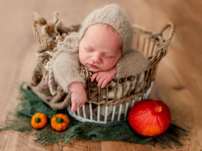 Newborn sleeping in basket next to ripe pumpkins