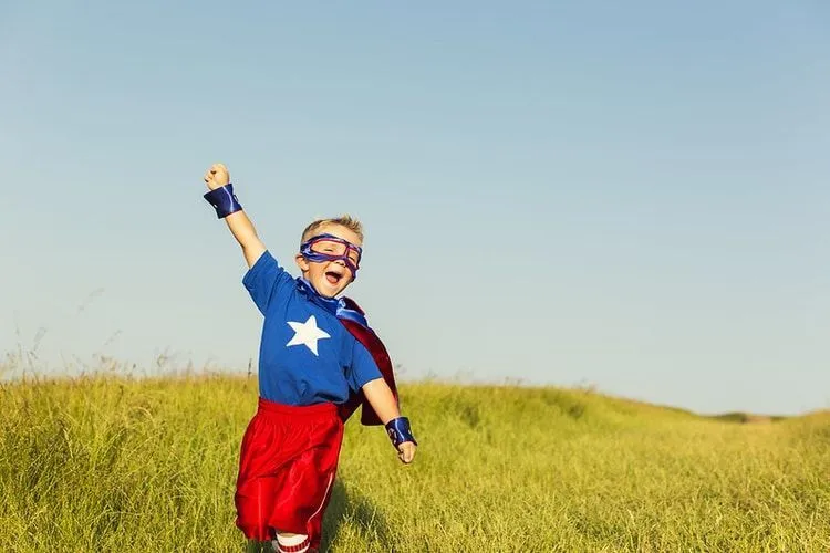 A little boy dressed as a superhero is posing in the meadow