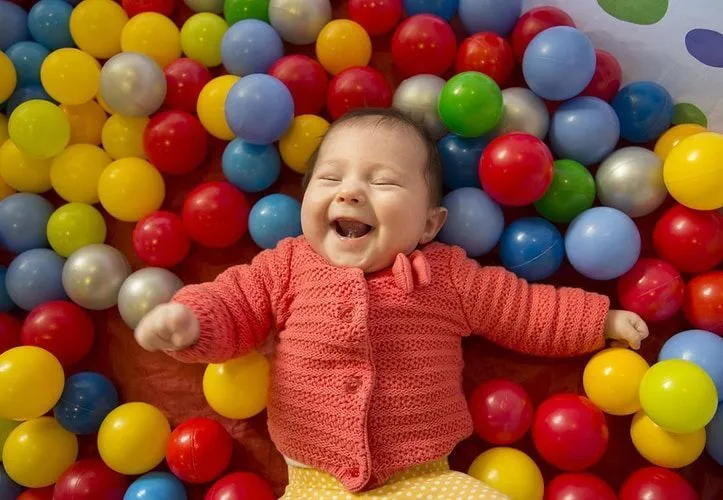 A baby girl laughing in a pool of colorful balls