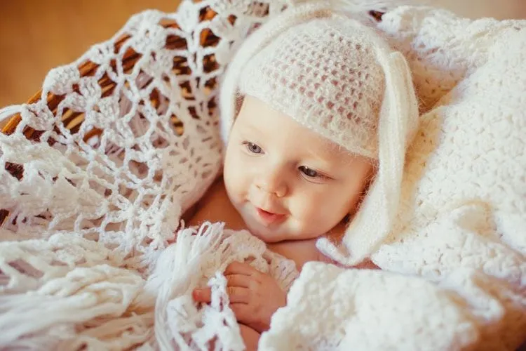 A newborn baby girl wearing white knitted hat lying in a white knitted basket