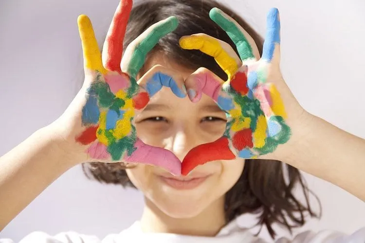 A young girl making heart sign with her painted hands