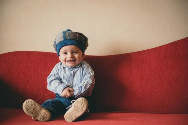 A Scottish baby boy sitting on a red sofa