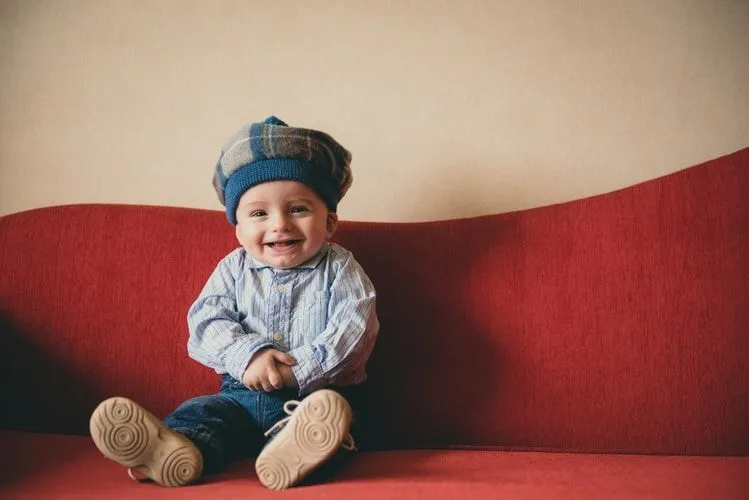 A little boy sitting on a red sofa wearing Scottish outfit