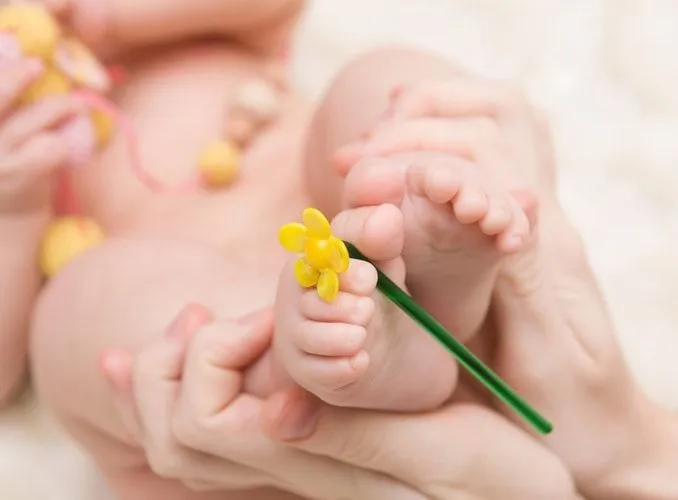 little baby feet with yellow flower in the mother's hands.