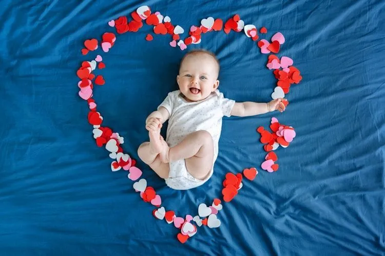 A newborn baby lying in the heart made up of tiny hearts on bed