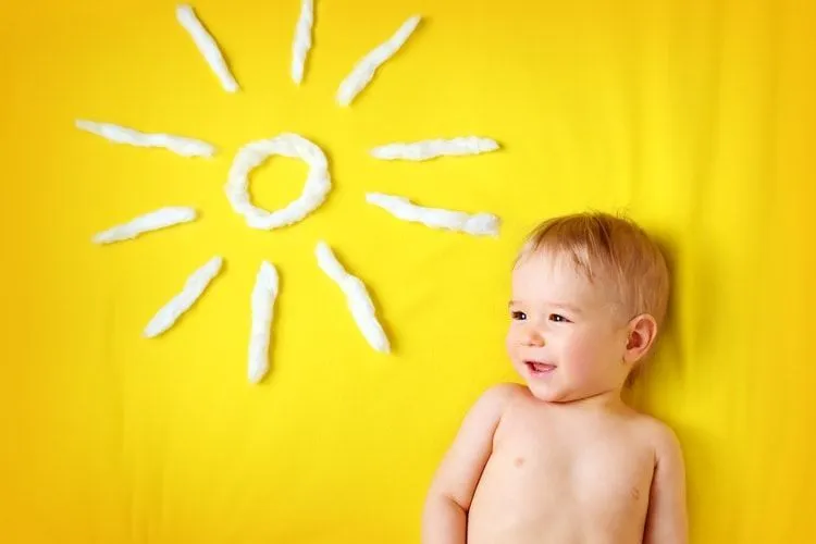 A newborn baby boy lying next to cotton sun on yellow background