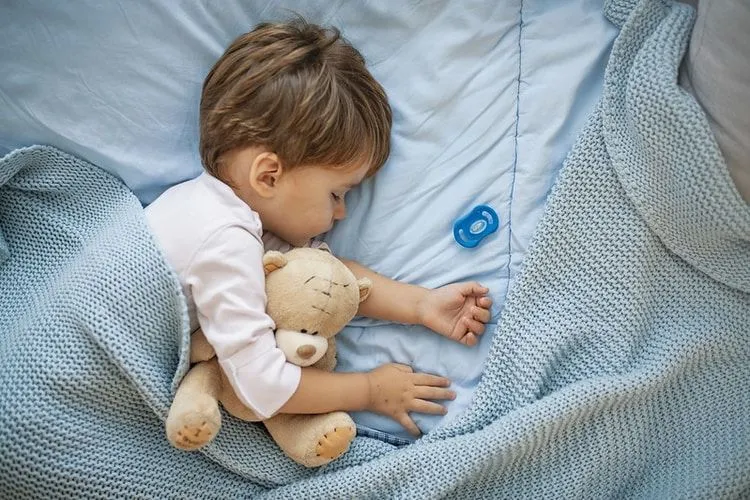 A baby boy sleeping with his teddy bear