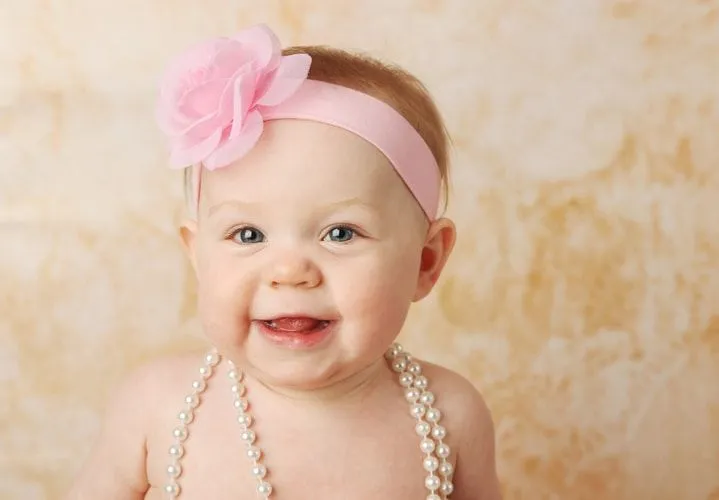 A newborn baby girl wearing pink headband and pearl necklace