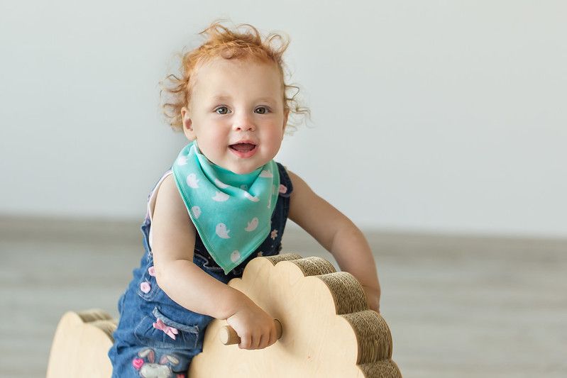 Cute infant baby wearing bib riding wooden toy.