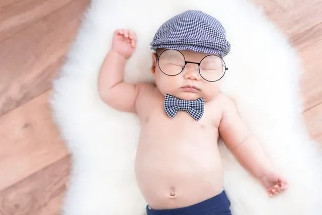 A newborn baby boy wearing a checkered cap and bow sleeping on white fur