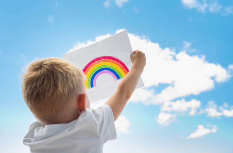 Little child holding up rainbow in the sky.