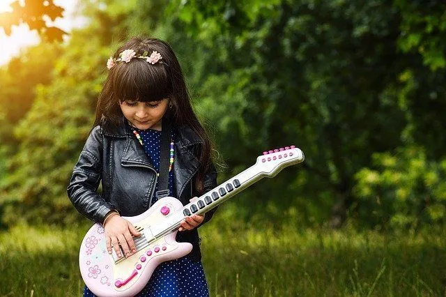 A little girl playing with her toy guitar in the park
