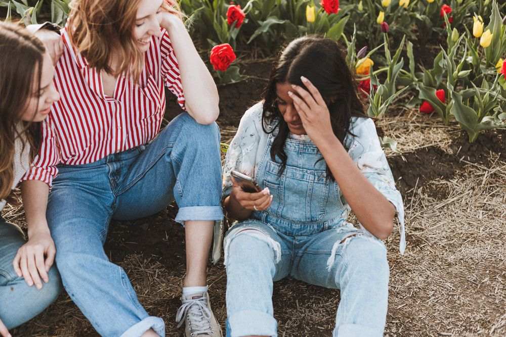 Three teenagers look at something funny on one of their phones.