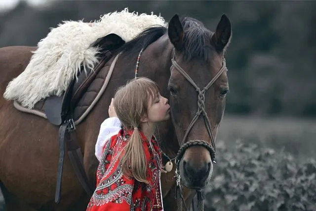 A little girl giving a kiss to a brown horse