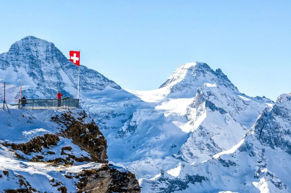 Swiss flag waving on mountain covered in white snow 