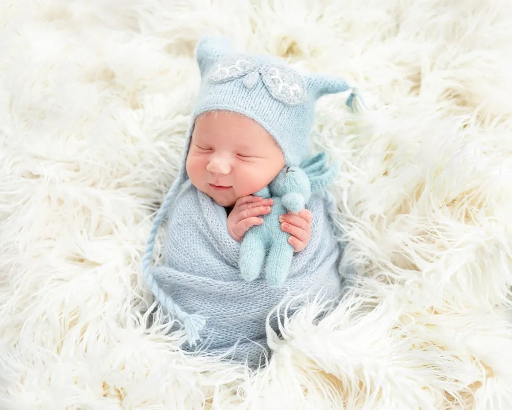 Adorable newborn baby wrapped in blue knitted clothes is holding a blue rabbit toy while sleeping