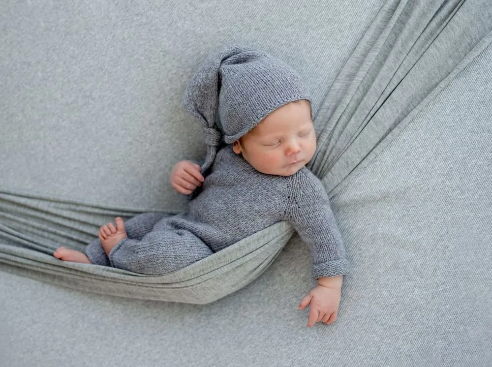 A newborn baby boy wearing grey clothes sleeping in grey swing