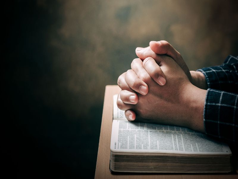 Man hands praying to god with the bible.