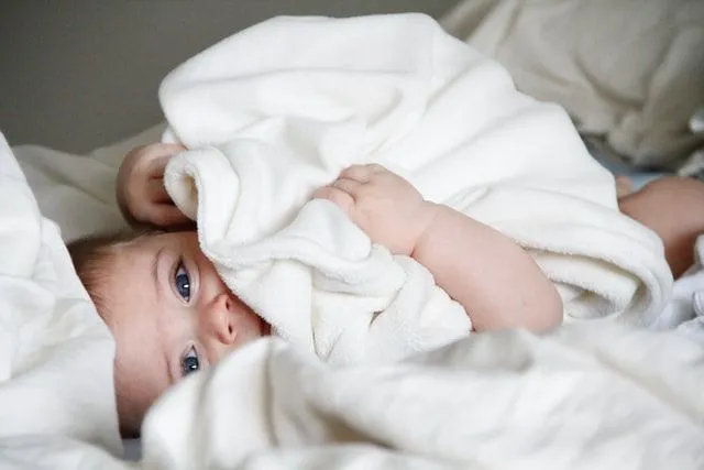 A baby lying in bed with white blanket