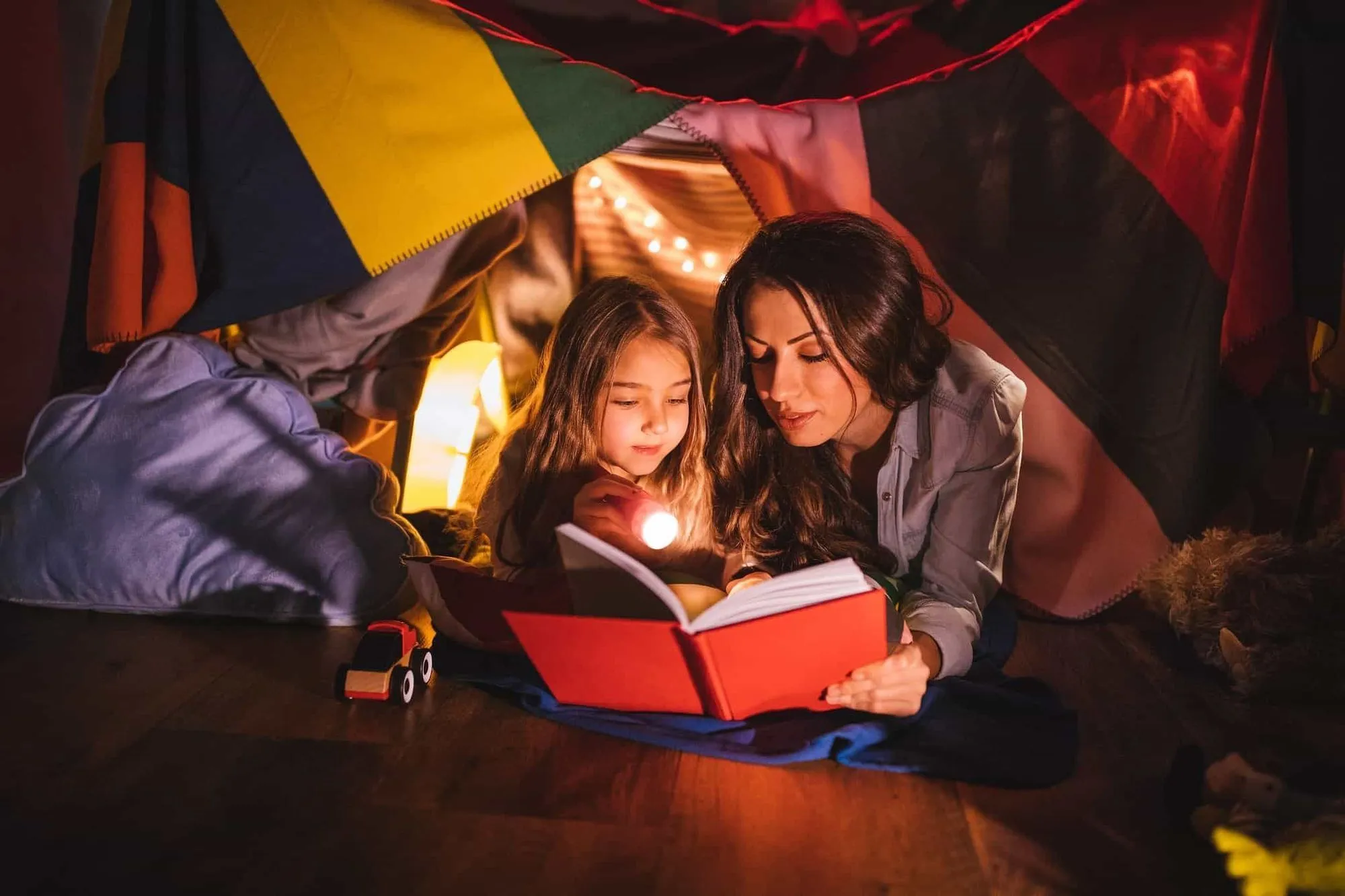 Mother and daughter in bedroom den reading a book together.