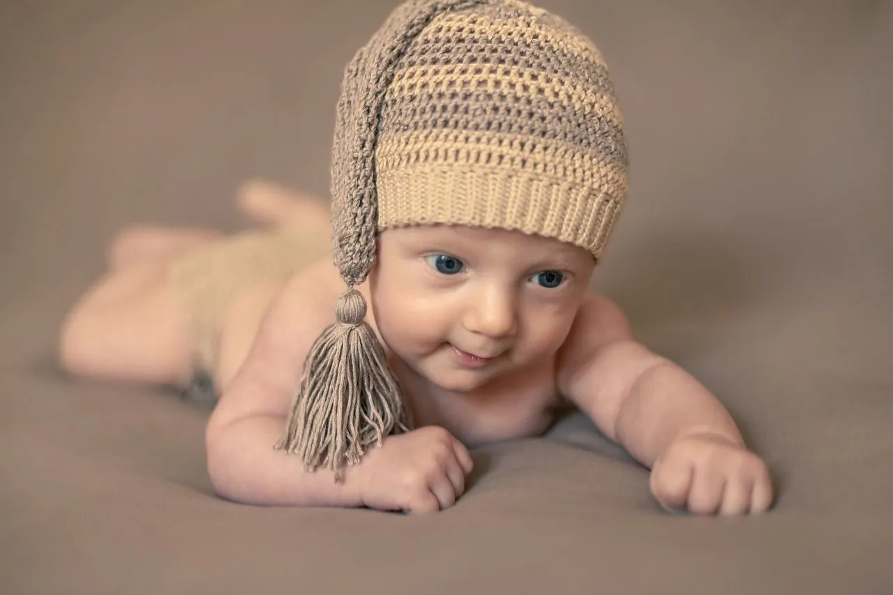 A newborn wearing a knitted hat crawling 