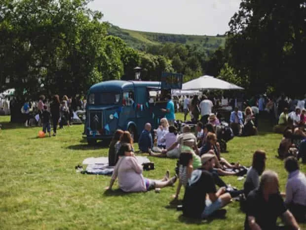 A group of people sitting on the grass at Firle Vintage Fair with vintage VW camper van in the background.