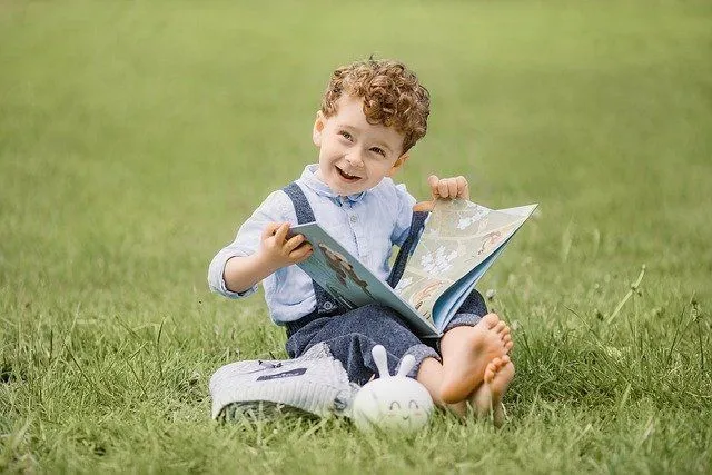 A little boy sitting on green grass with a book in his hands