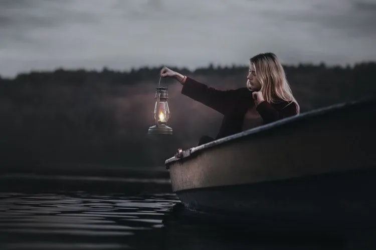 A girl holding lamp while sitting in a boat at night