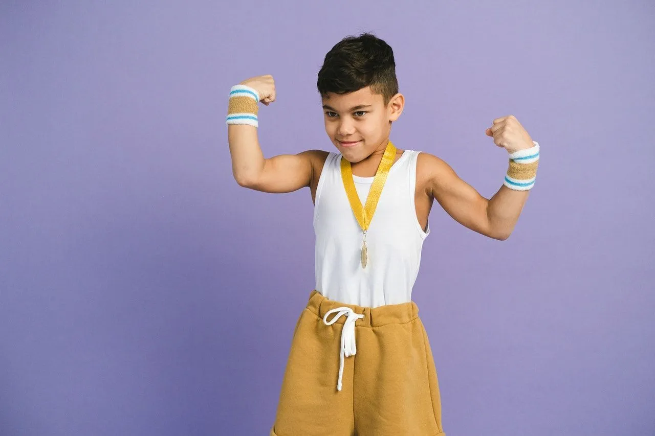 A little boy flexing his biceps after winning a gold medal