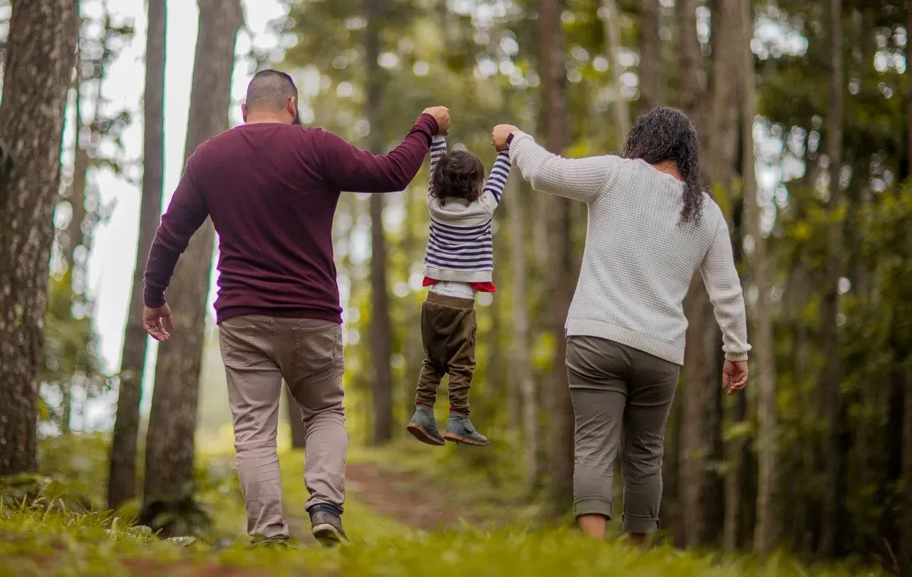 Parents holding hands and lifting their little kid in the air while walking in the forest