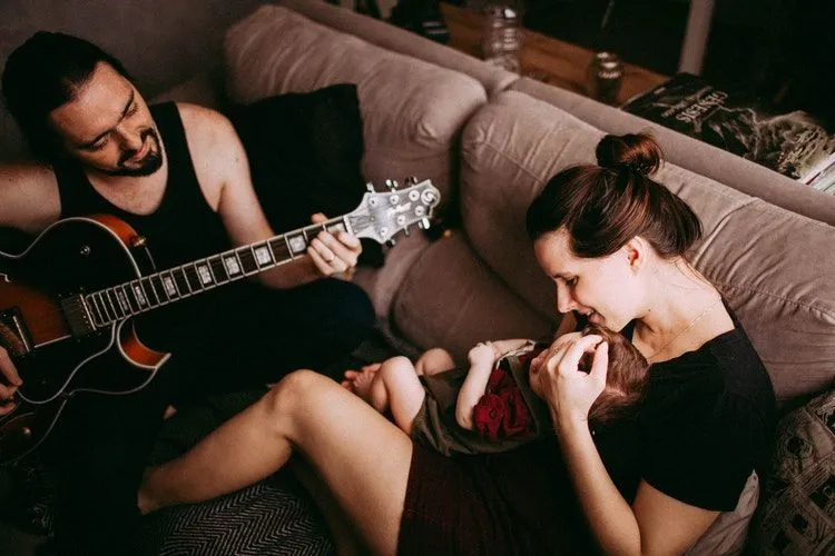 A man playing guitar in front of his wife and baby