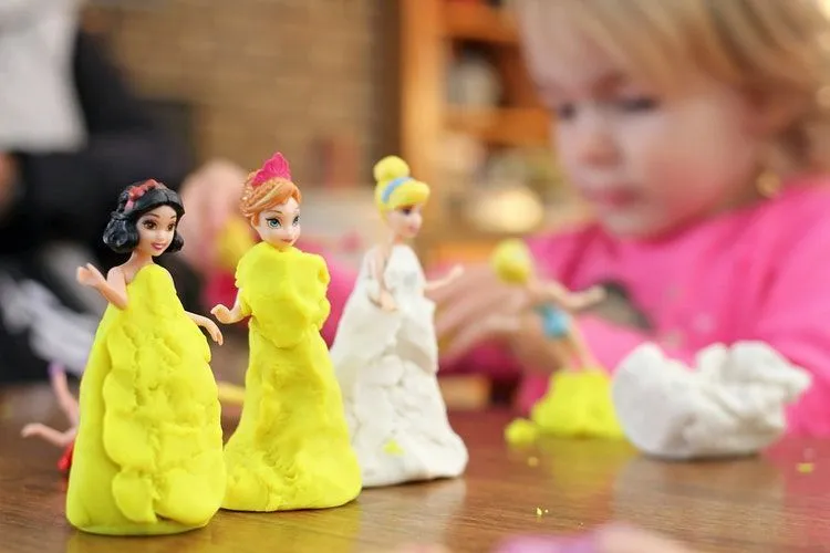 A little girl making clay dresses for her princess figurines