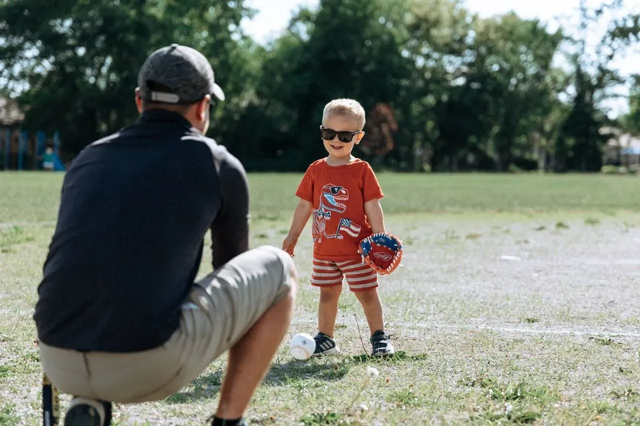 A little boy wearing sunglasses and gloves playing with his father