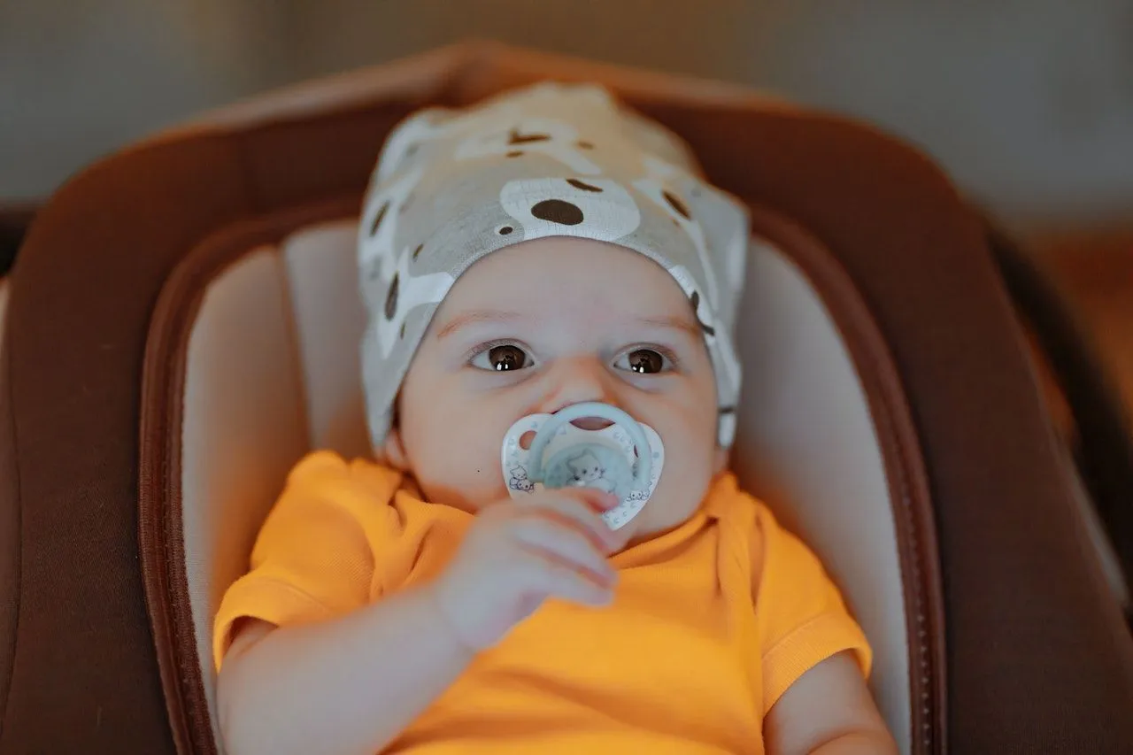 A newborn baby wearing orange clothes nibbling 