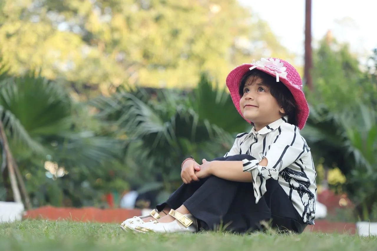 An Indian girl wearing pink hat is sitting in a garden