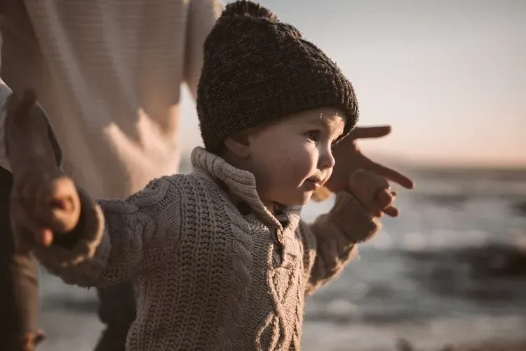 A baby boy learning to walk with the help of his parent on beach