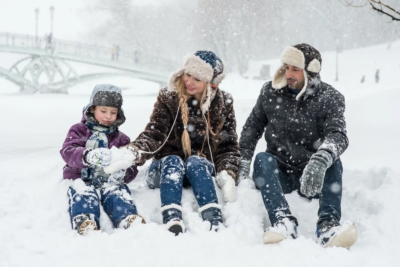 Parents with their son enjoying snowfall outdoor in the park