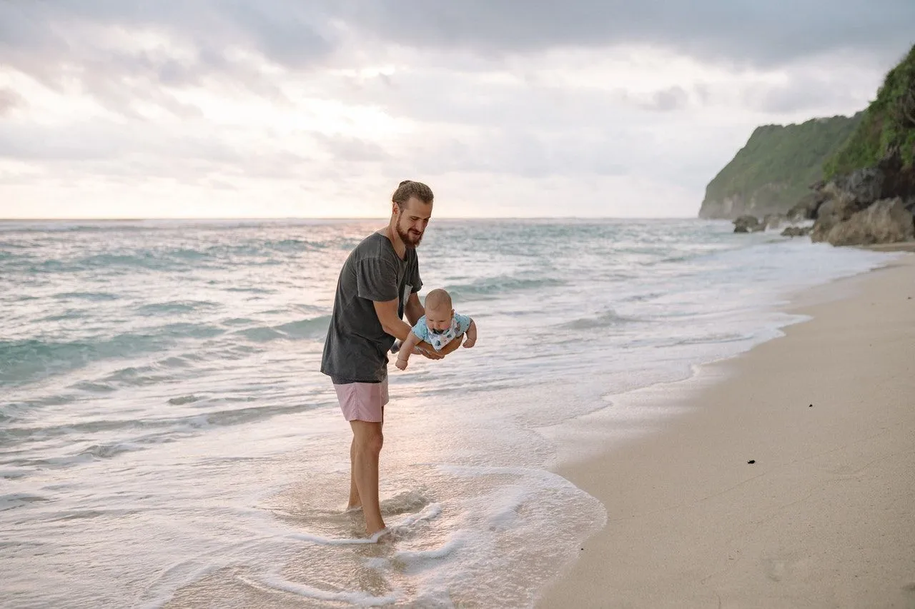 A dad playing with his newborn baby on the beach