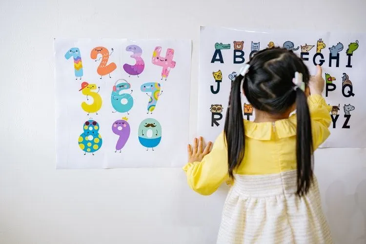 A girl learning alphabets from a chart on wall