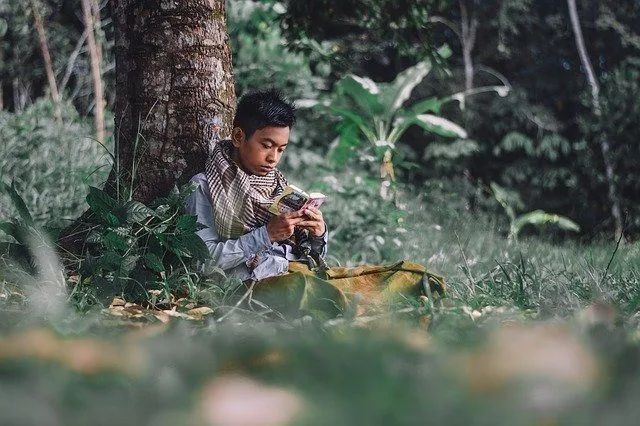 A boy reading religious book sitting under a tree