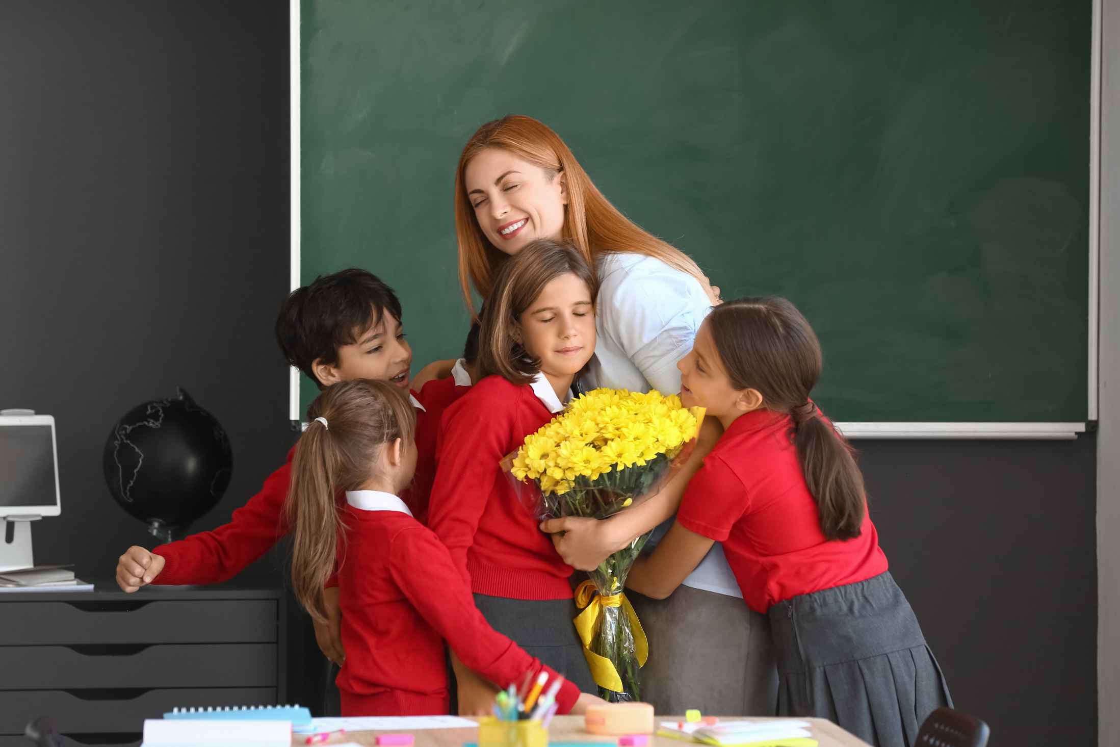 School children wishing their teacher in classroom with yellow flowers