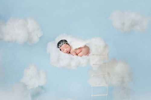 Adorable baby sleeping on clouds in blue sky like little angel.