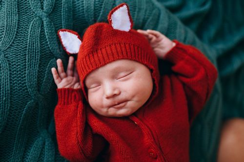 A newborn adorable baby in red costume sleeping on green blanket
