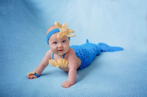 Newborn baby ggirl in a mermaid costume on a blue background
