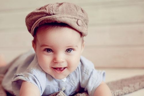 The baby in the hat smiling looking at camera.