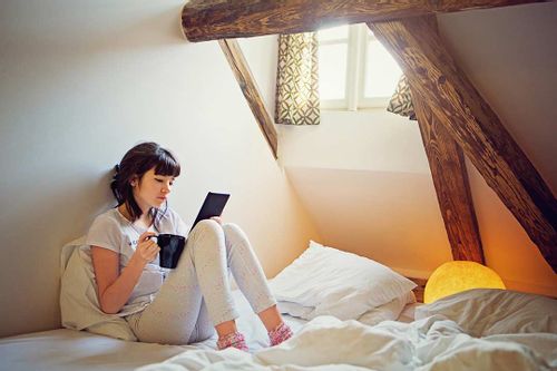 A teenage girl relaxing on her bed reading a story.
