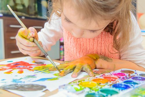 Young girl enjoying messy play and painting on her hand.