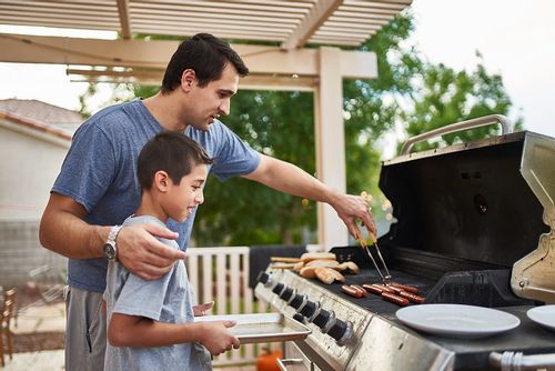 Father showing his son how to cook using the BBQ.