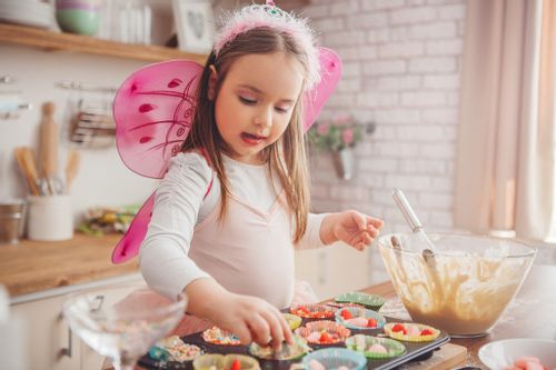 Young girl dressed as a fairy baking rainbow-inspired food.